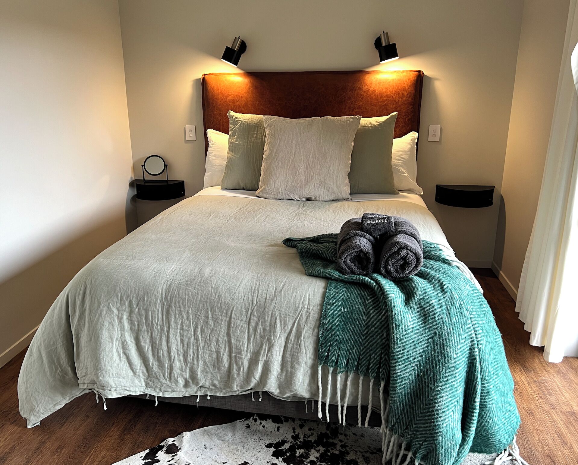 Un lit bien fait, avec une couette blanche et des oreillers, un plaid vert et une paire de serviettes enroulées posées sur le lit.