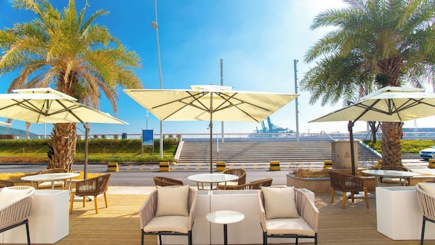 An outdoor seating area with tables and chairs, umbrellas, and palm trees. - StarChain Ocean View Hotel (Shenzhen Yantian Seafood Street) (Shenzhen)
