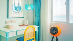 A room with a white desk, a yellow chair, a framed artwork, a blue curtain, and a view of the sea through a window. - StarChain Ocean View Hotel (Shenzhen Yantian Seafood Street) (Shenzhen)