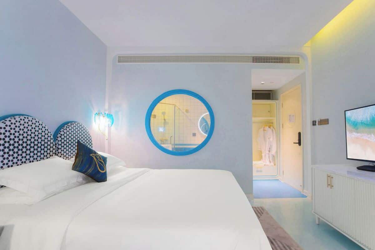 A hotel room with a large bed, a round mirror, a television, and a view of the bathroom.