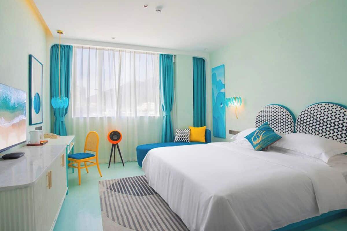 A hotel room with a bed, a desk with a TV, a chair, a small table, and curtains.