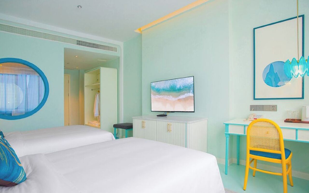 Habitación de hotel con dos camas, un escritorio, una silla, un televisor y un cuadro en la pared.
