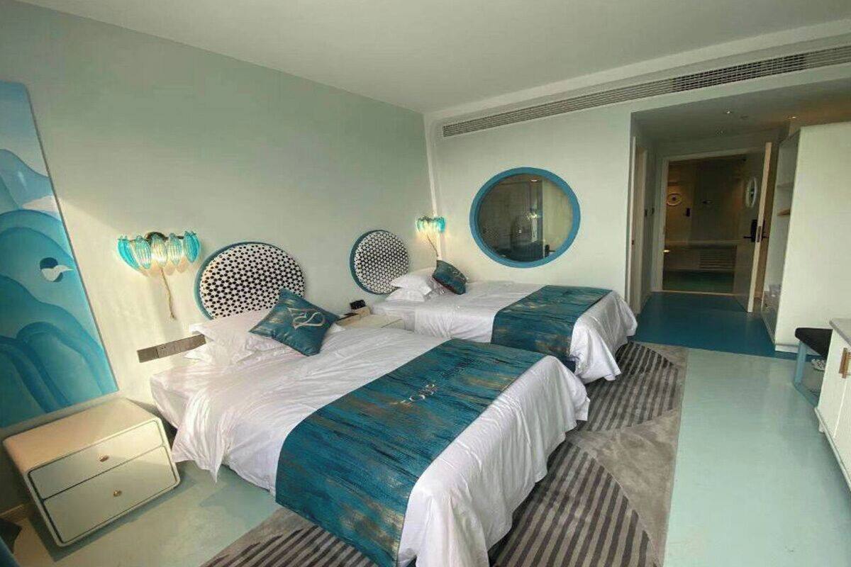 A hotel room with two beds, a round mirror, a nightstand, and a bathroom visible through an open door.