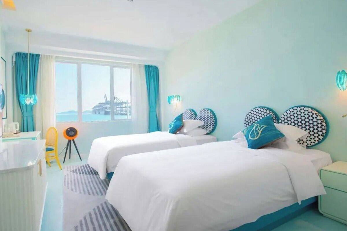 A hotel room with two beds, a desk, a chair, and a view of a bridge.