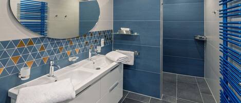 Een moderne badkamer met een witte wastafel, een ronde spiegel en een douchegedeelte met blauwe tegels.