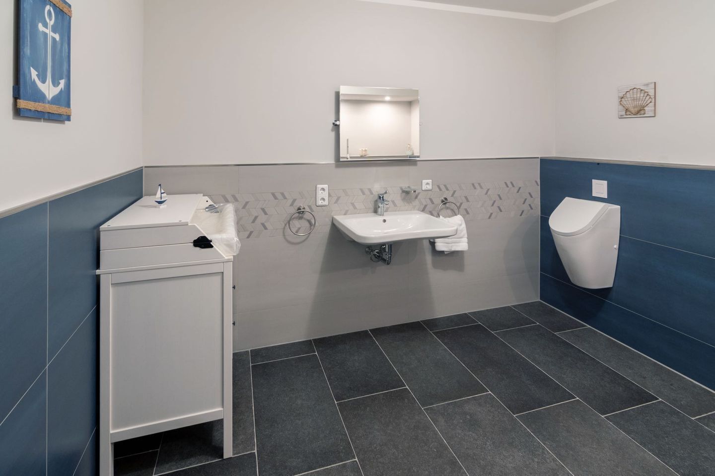 A modern bathroom with a white sink, a mirror, a toilet, and a small cabinet.