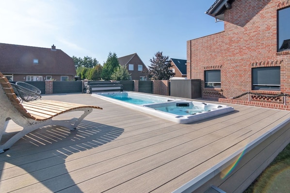 A backyard with a wooden deck, a hot tub, and a lounge chair.