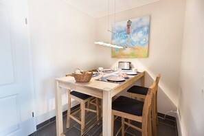 Et spiseområde med et træbord dækket til to personer, en kurv og et maleri af et fyrtårn på væggen.