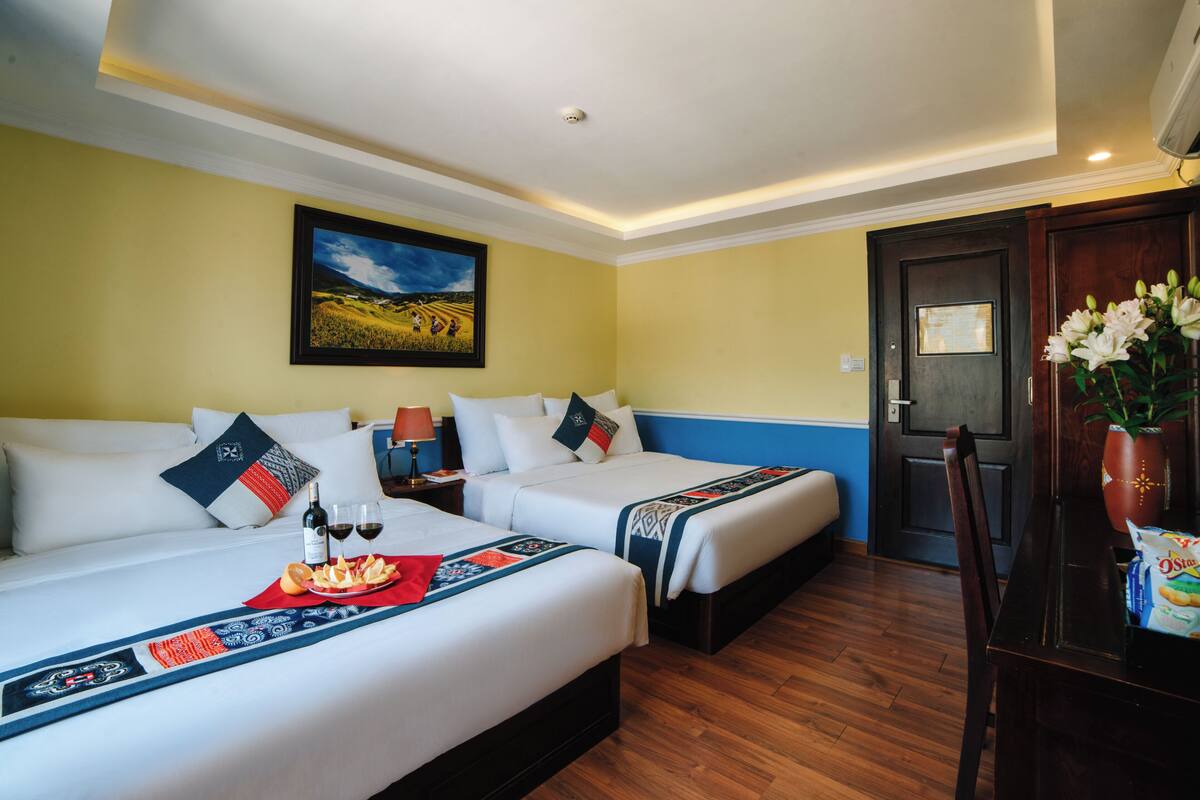 Ein Hotelzimmer mit zwei Betten, Holzboden, einem Bild an der Wand und einer Tür mit Holzrahmen.