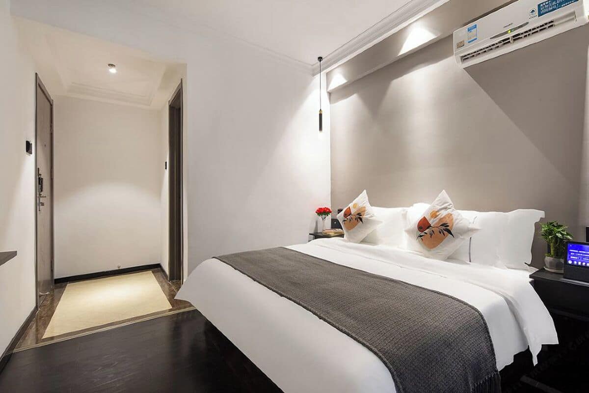 Habitación de hotel con cama, mesita de noche y aire acondicionado de pared.