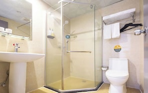 Un baño con ducha envuelta en vidrio, un lavamanos, un inodoro y un perchero para toallas.