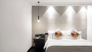 A modern hotel room with a neatly made bed, a bedside table with a lamp, and a wall-mounted light fixture. - Starchain Heehee Hotel - Sanya Bay Walking Street Store (Sanya)