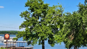 Un muelle con un cartel de Texaco, un embarcadero de madera y un árbol grande frente a un lago tranquilo.