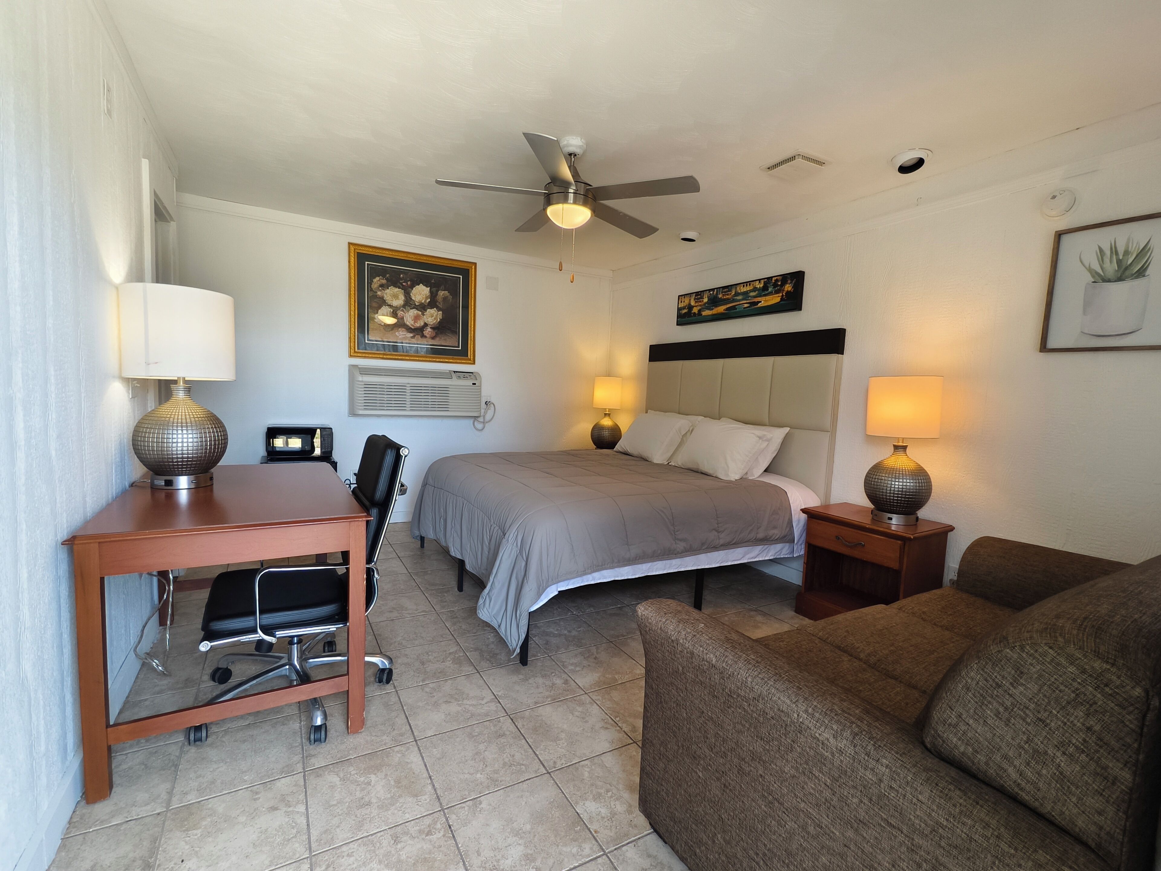 A hotel room with a bed, desk, chair, and a ceiling fan.