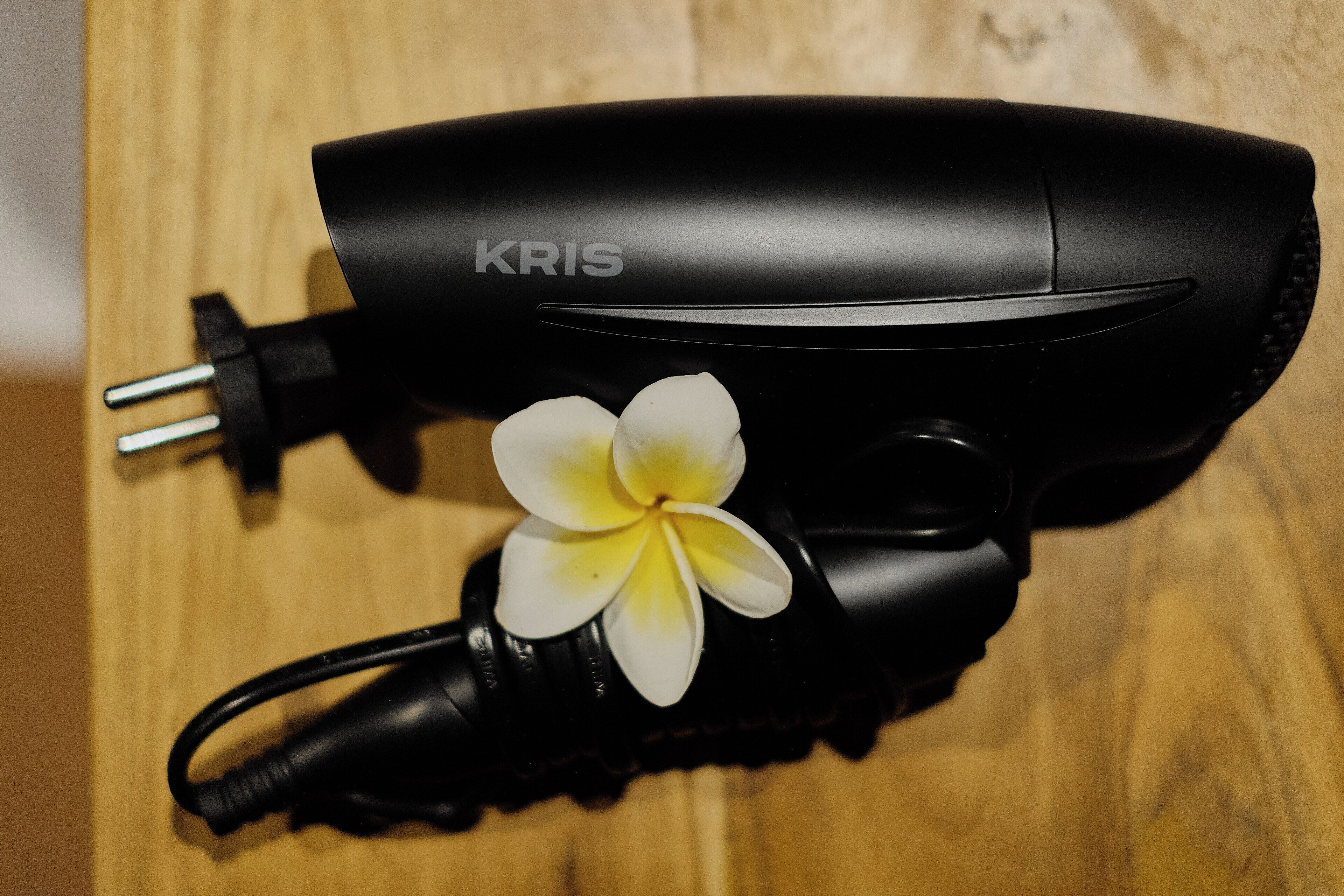Un sèche-cheveux noir de la marque « KRIS », posé sur une surface en bois.