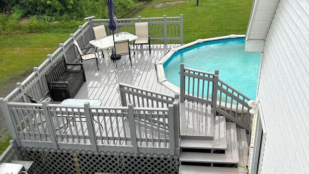 A wooden deck with a pool, outdoor furniture, and a grill.