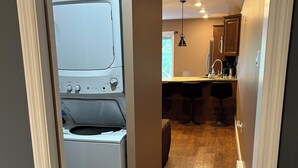 A laundry room with stacked washers and dryers, a kitchen area with bar stools, and a wooden floor.