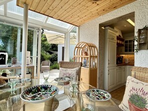 Un luminoso soggiorno e sala da pranzo open space con tavolo in vetro, mobili in vimini e vista sul giardino.