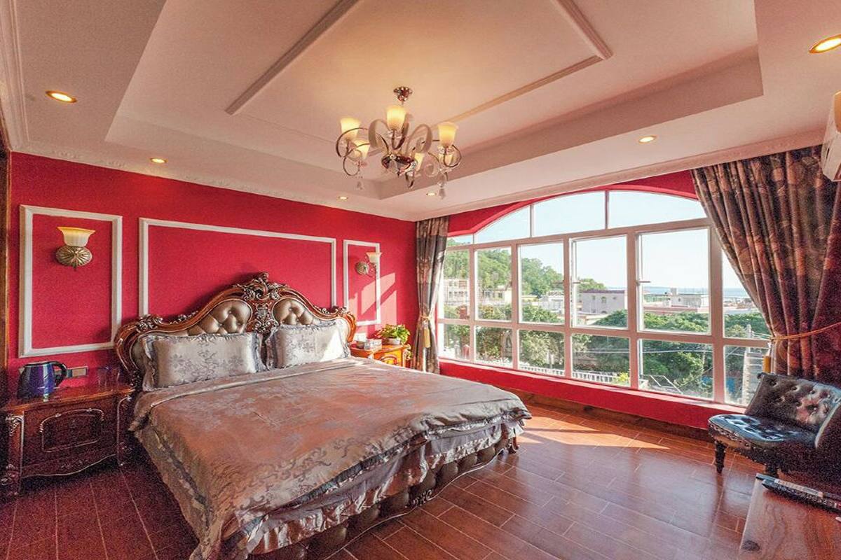 A spacious bedroom with a large bed, a chandelier, and a view of the city through a large window.