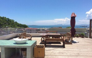 Une terrasse avec une table et des chaises, un grand parasol et une vue sur la mer et les montagnes.