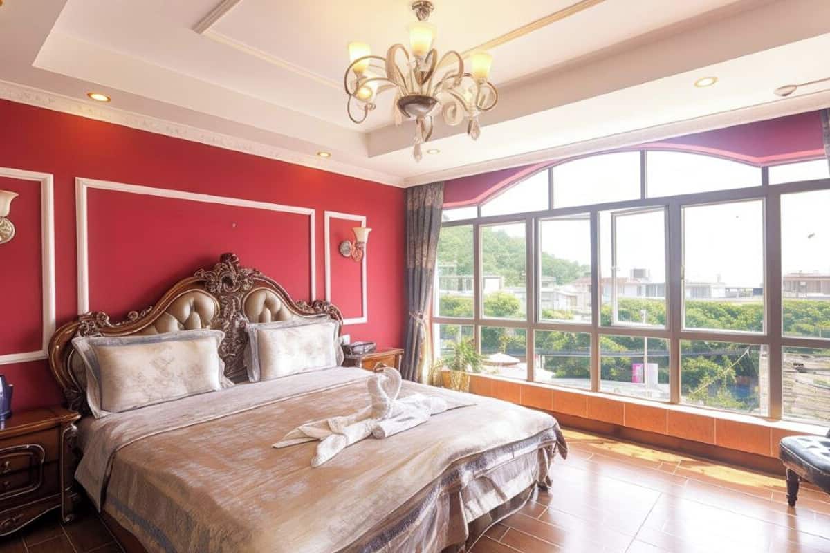 A spacious bedroom with a large bed, a chandelier, and a view of the city through large windows.