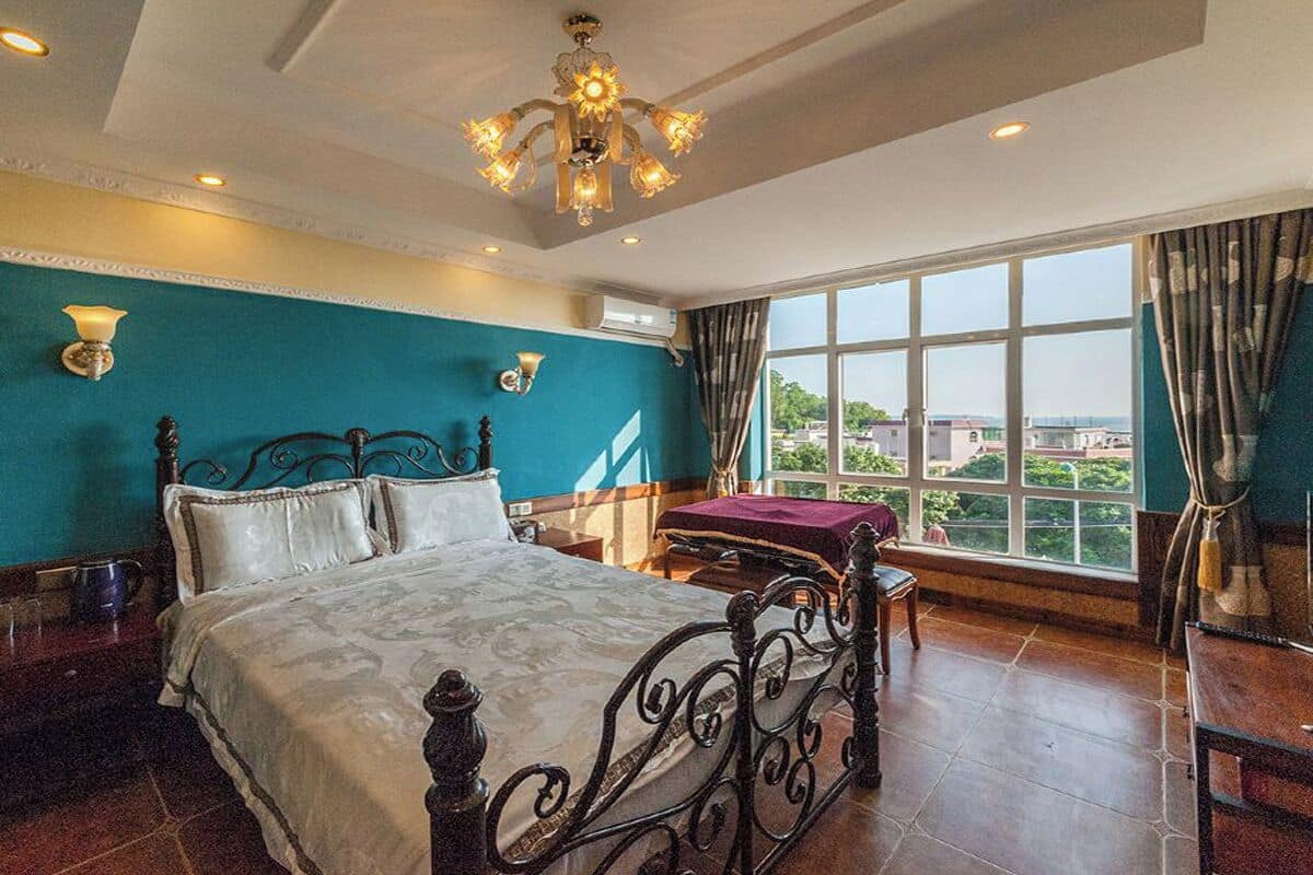 A bedroom with a large bed, a chandelier, a view of the city, and a window with curtains.