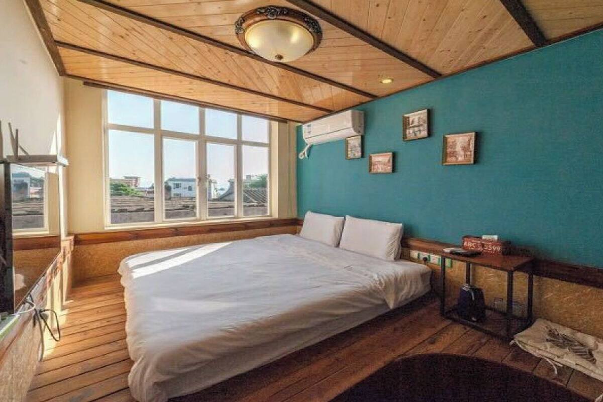 A room with a large bed, wooden flooring, a window with a view, and a teal accent wall.