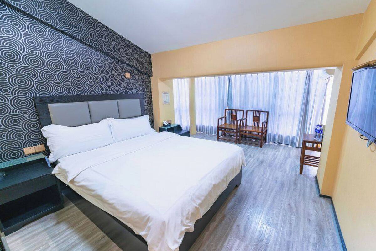 Ein Hotelzimmer mit einem großen Bett, einem Schreibtisch mit Stuhl, einem an der Wand montierten Fernseher und einem Balkon mit Vorhängen.