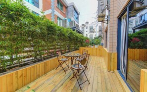 A wooden deck with a table and chairs, surrounded by a bamboo fence and potted plants.