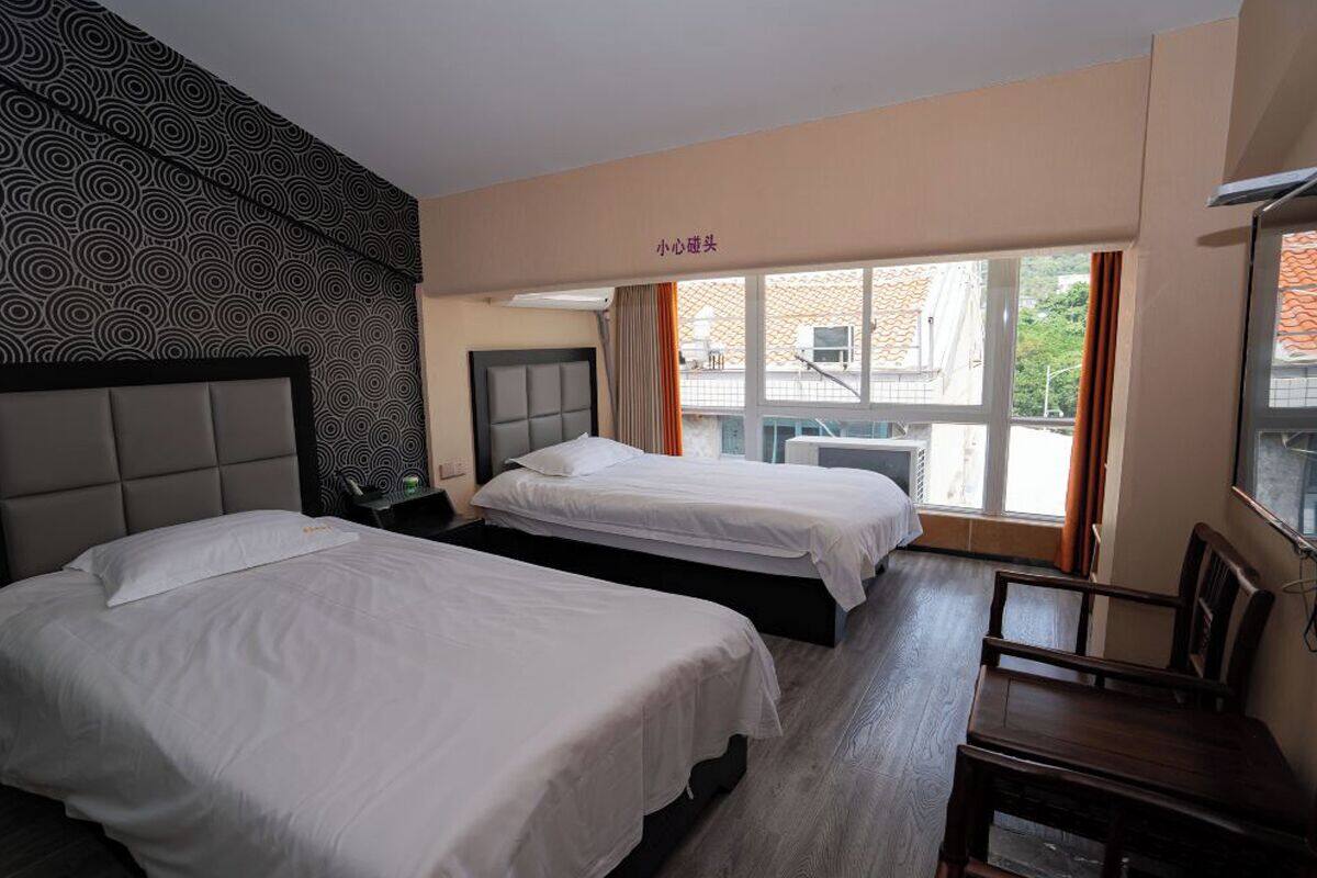 Ein Hotelzimmer mit zwei Betten, einem Holztisch und einem Fenster mit Vorhängen.