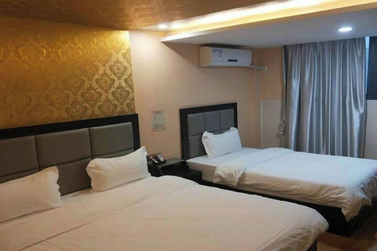 Ein Hotelzimmer mit zwei Betten, einem Kopfteil, einer Klimaanlage und einem Vorhang.