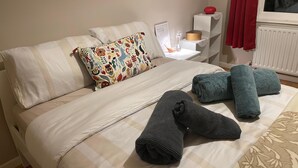 A neatly made bed with white linens, a colorful floral pillow, and rolled towels.
