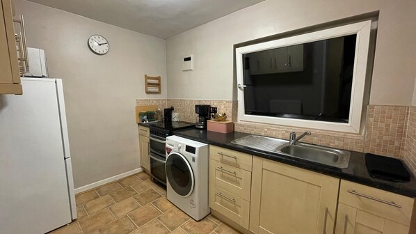 A compact kitchen with a washing machine, a refrigerator, a coffee maker, and a window above the sink.
