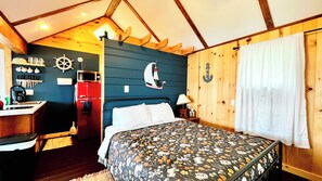 A bedroom with a bed, a red appliance, nautical wall decor, and a window with curtains. - Lakefront Cabin w/ Dock & Kayaks, Fishing Escape
Marine Comfort - Cabin 8 (South Haven)