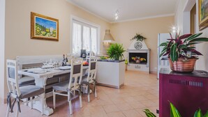 A dining area with a table set for four, a kitchen in the background, and a fireplace with plants. - Gerry House by Interhome (Camaiore)