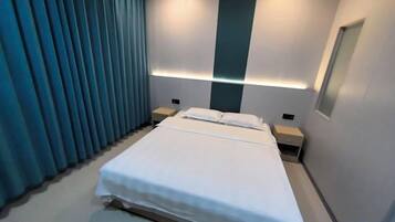A modern hotel room with a large bed, bedside tables, and a wall-mounted light fixture.