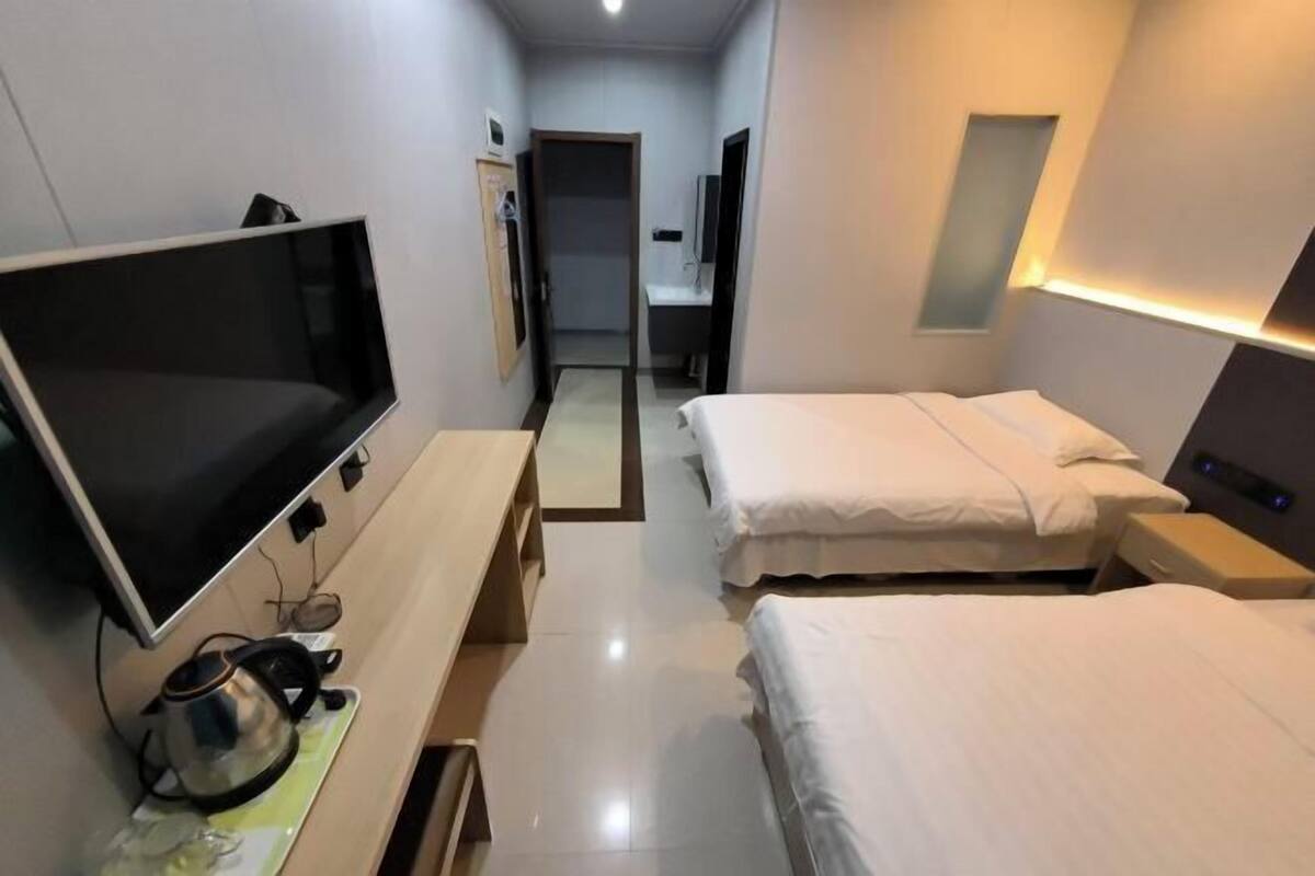 Une chambre d’hôtel équipée d’une télévision à écran plat, d’une bouilloire, de deux lits, d’une table de chevet et d’un miroir.