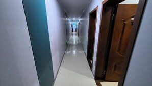 Un couloir étroit et bien éclairé, doté d’un sol carrelé et de portes en bois d’un seul côté.