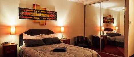 A hotel room with a large bed, a ceiling fan, a mirror, and artwork on the wall.
