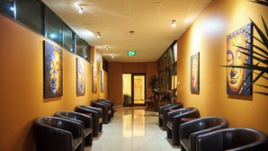 A hotel lobby with rows of black leather chairs, a tiled floor, and artwork on the walls. - Mirambeena Motel (Whyalla)