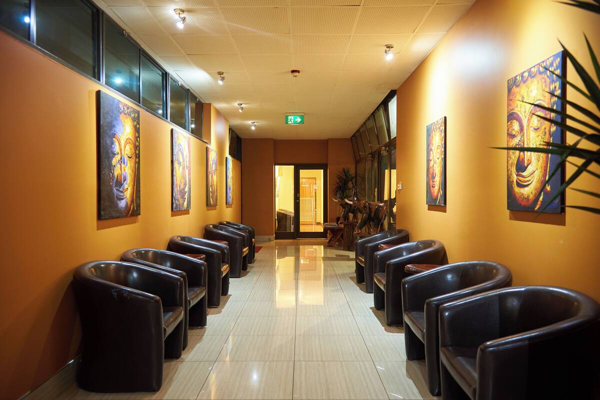 Un hall d’hôtel avec des rangées de fauteuils en cuir noir, un sol carrelé et des œuvres d’art accrochées aux murs.