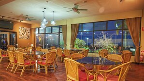 A dining area with wicker chairs and tables, large windows with curtains, ceiling fans, and a wall-mounted TV. - Mirambeena Motel (Whyalla)