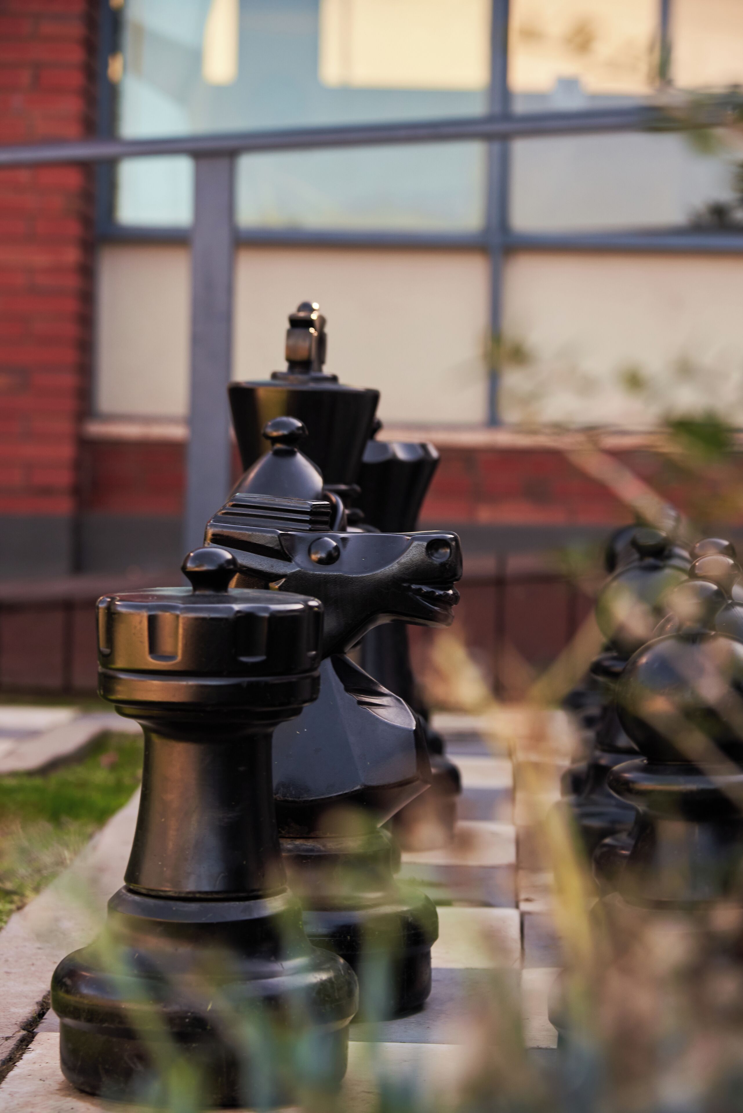 Chess pieces on a board outside a building with a large window.