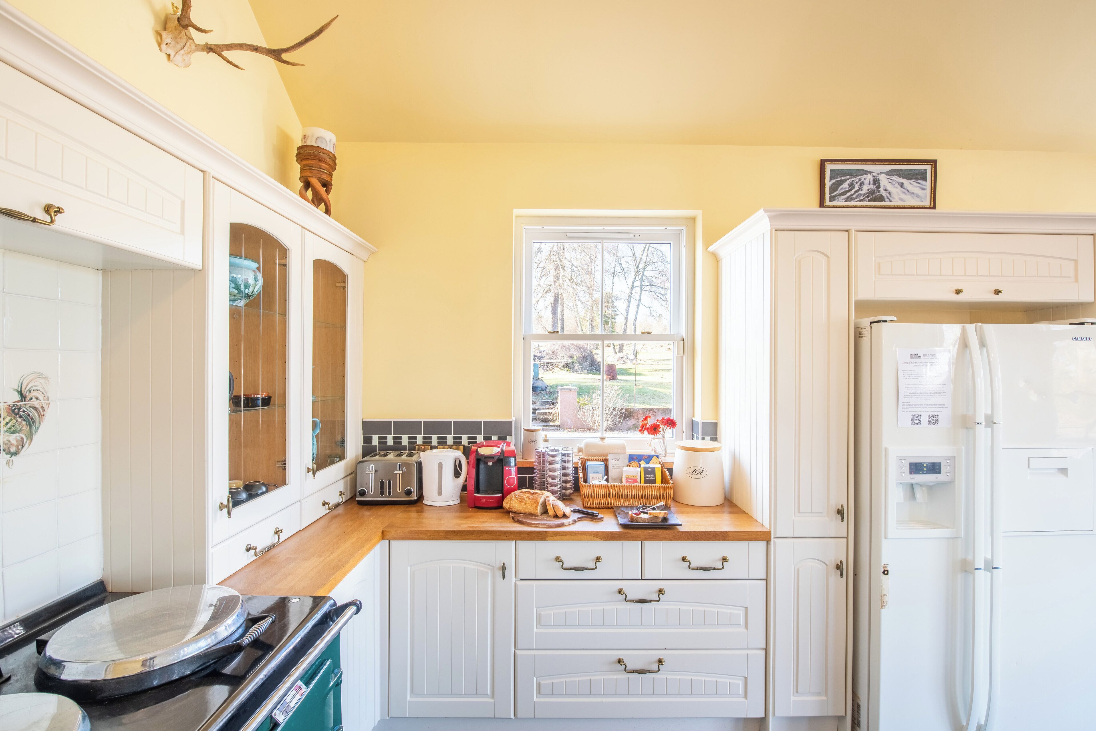 A kitchen with white cabinets, a window, a refrigerator, and various appliances.