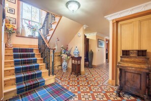 Un escalier recouvert d’une moquette à carreaux, une rampe en bois et un vase rempli de fleurs.