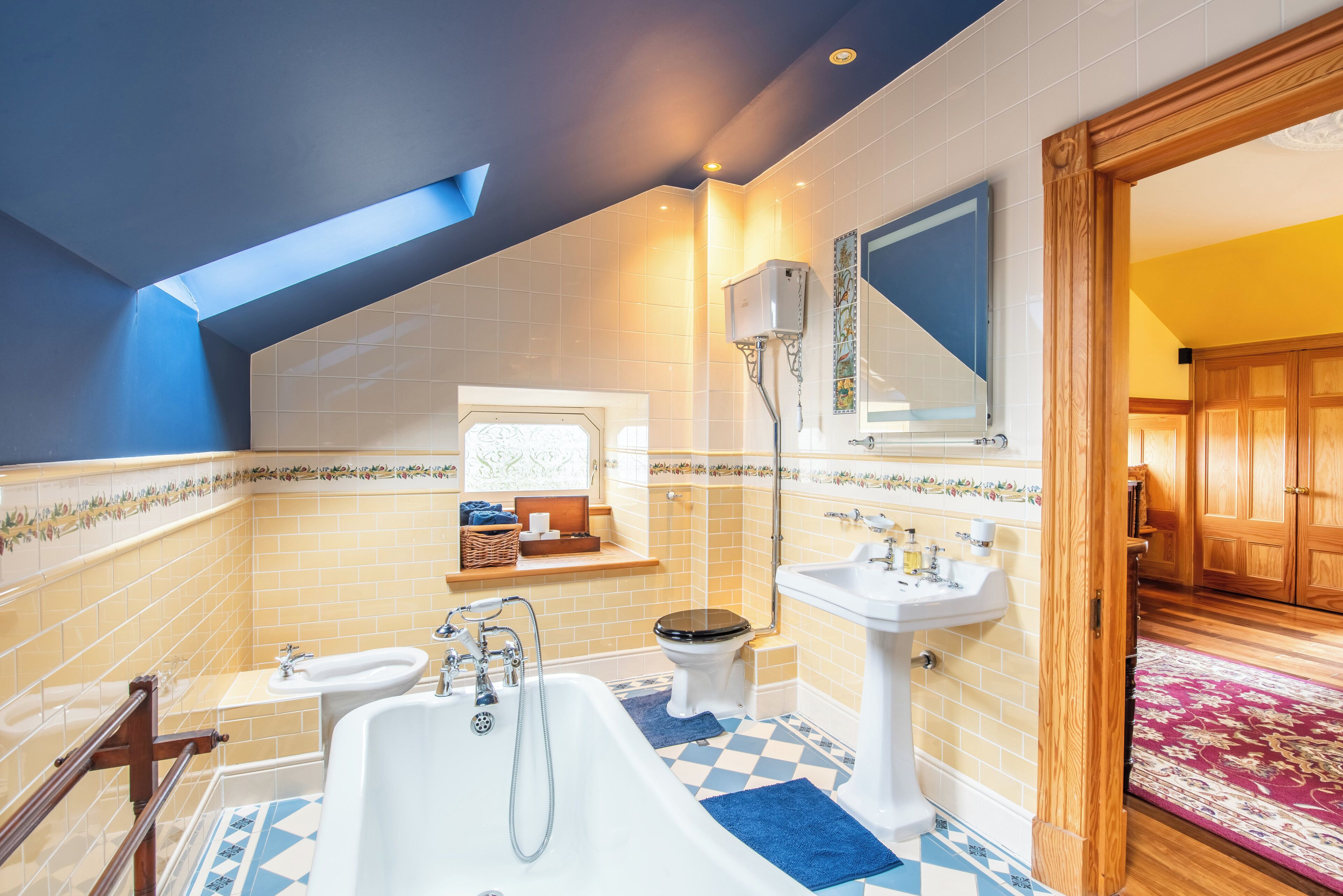 A bathroom with a bathtub, two sinks, a toilet, and a skylight.