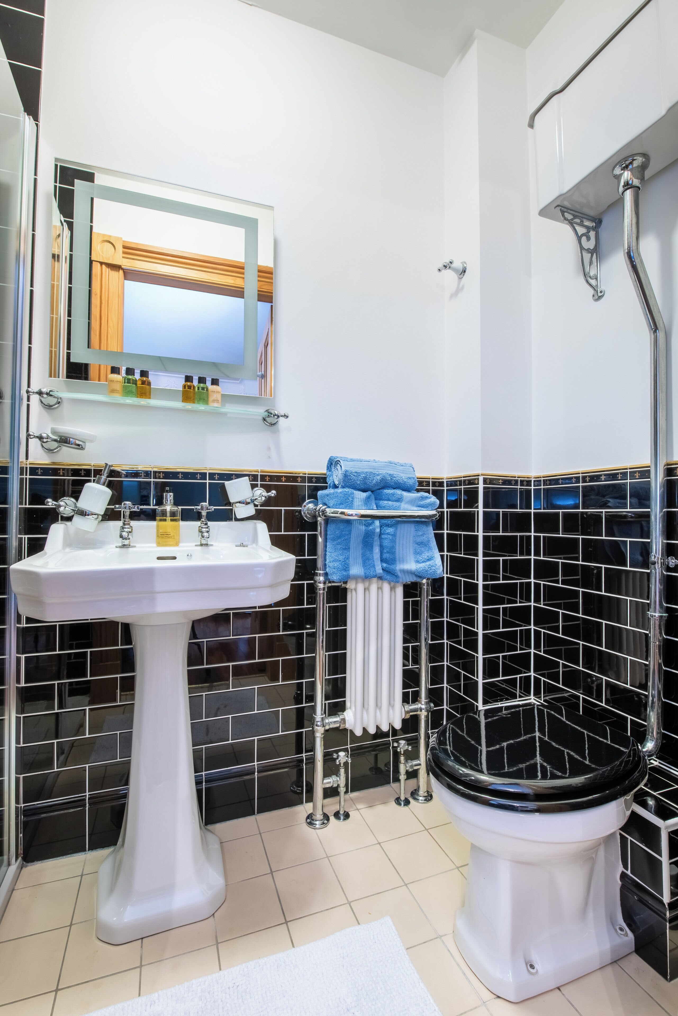 Une salle de bain avec un lavabo sur colonne blanc, des toilettes noires, une douche en verre et un miroir au-dessus du lavabo.