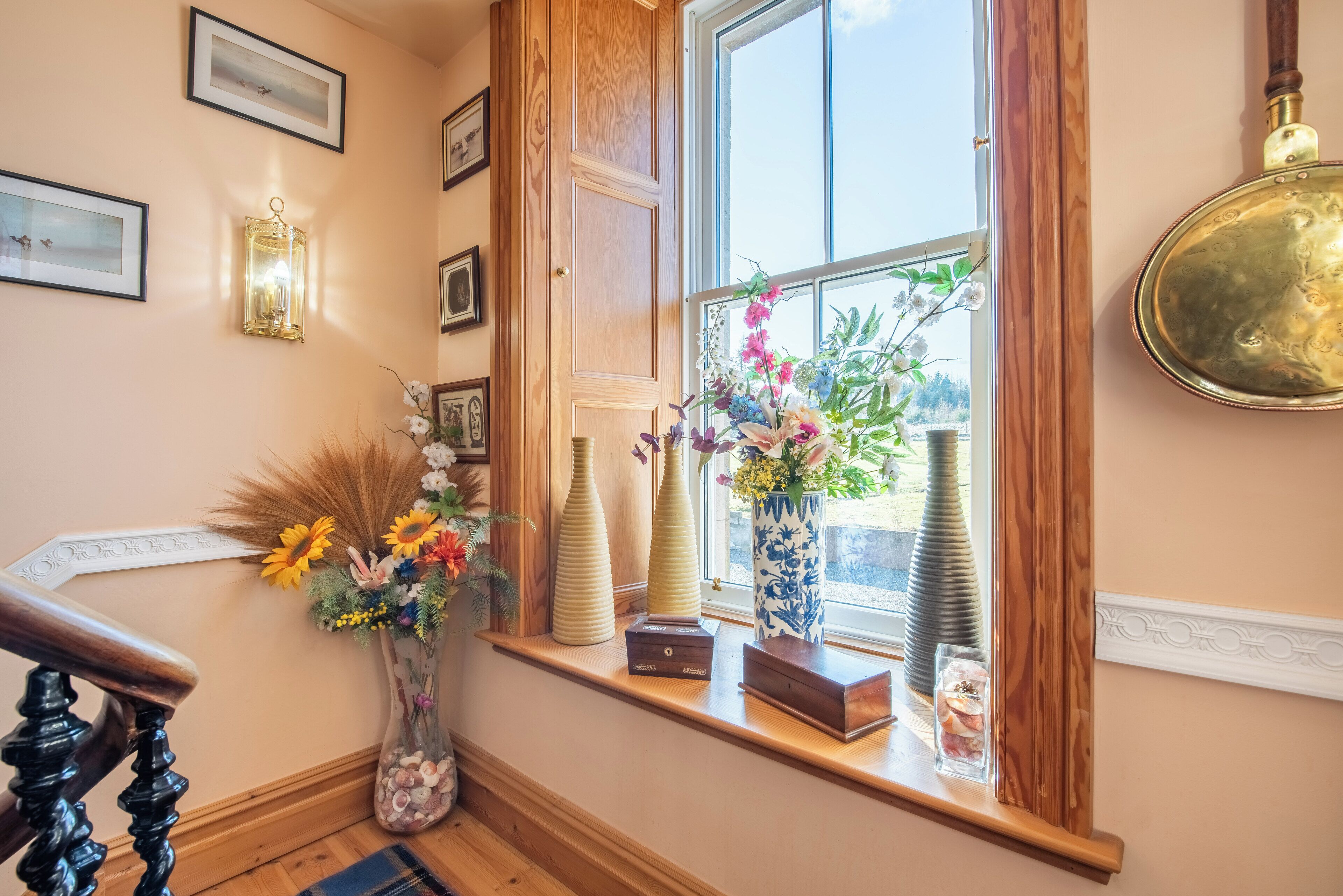 A staircase with a wooden handrail, a window with a view of greenery, and various decorative items on the windowsill.