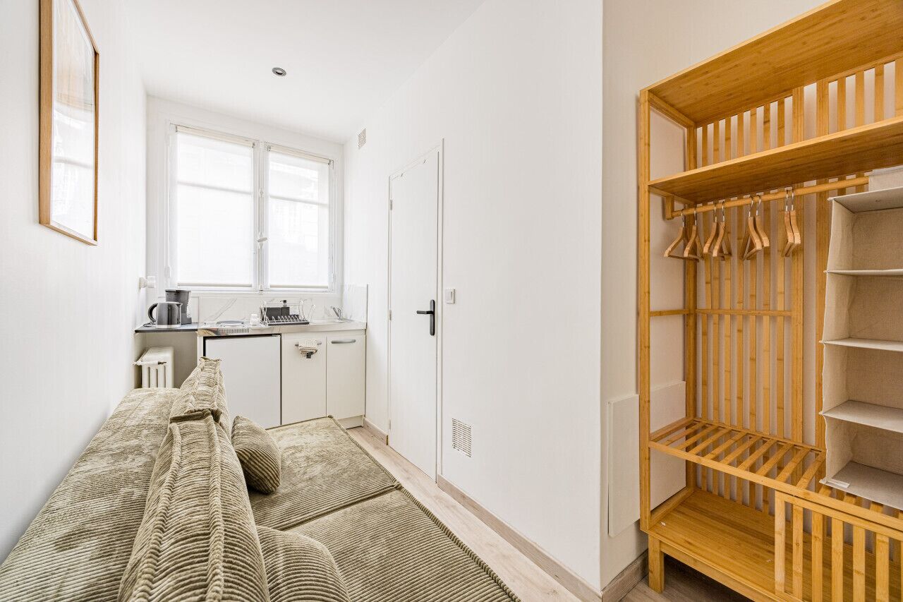 A compact living space with a kitchenette, a wooden wardrobe, and a sofa.