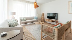 Een moderne woonkamer met een bank, een salontafel, een televisie en een rieten stoel.